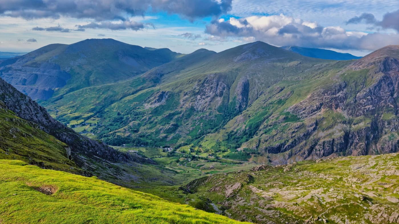 A steep-sided Welsh valley, grassy slopes in the foreground falling away to a ridge of peaks beyond.