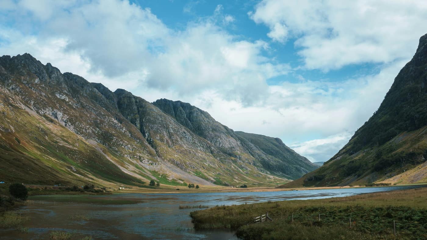 A long rocky ridge running high above a Highland glen, with a shallow river winding across the flat glen floor below.