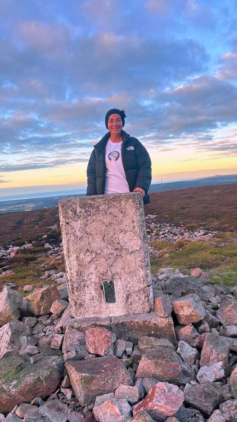 Katrina at the trig point, the sunset behind her