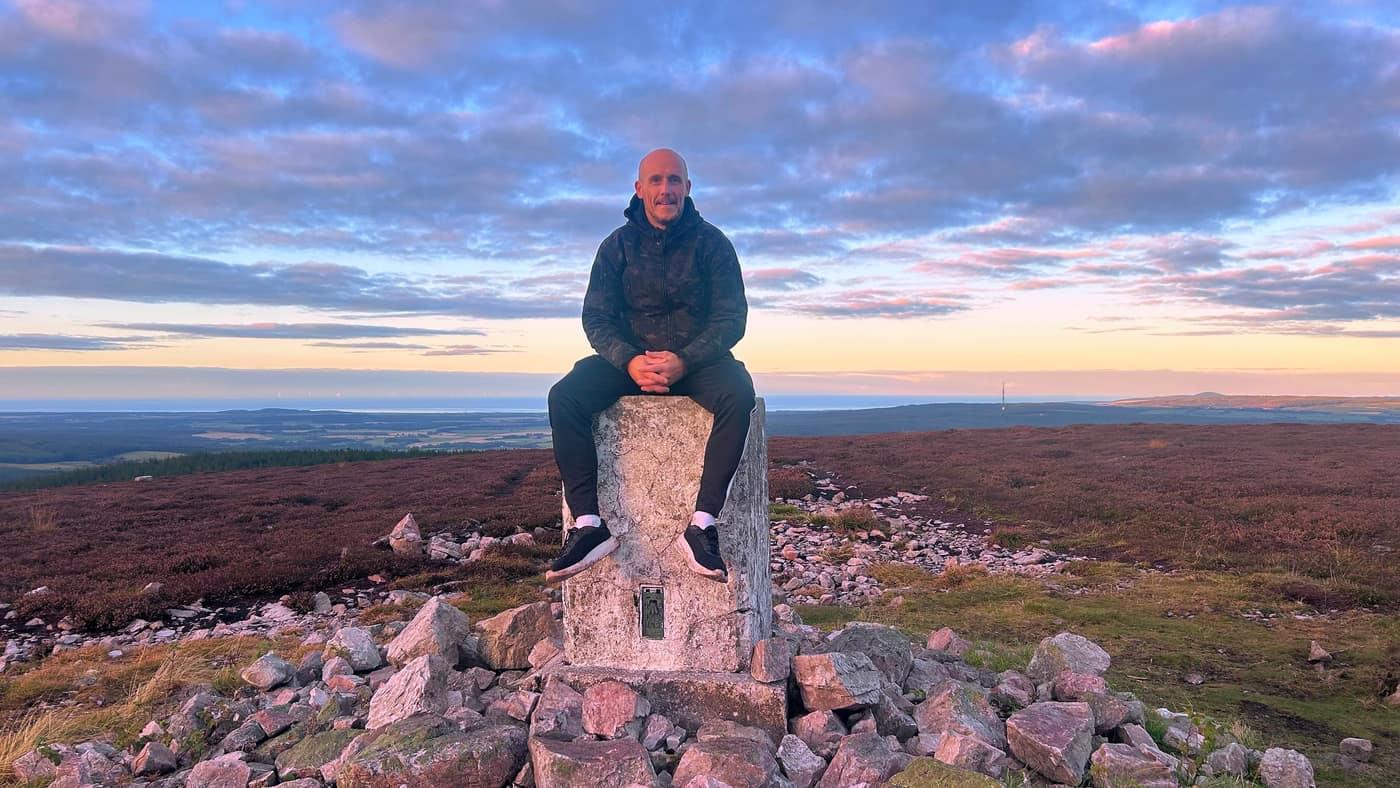 Ross sitting on the trig point, the Firth behind him
