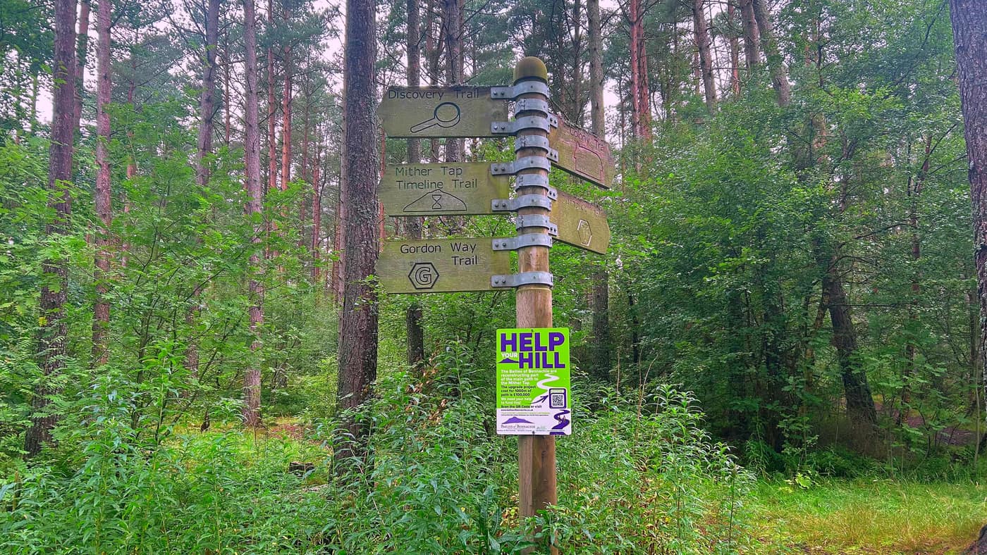 A wooden fingerpost with the Discovery, Mither Tap Timeline, Colony and Gordon Way trails on it