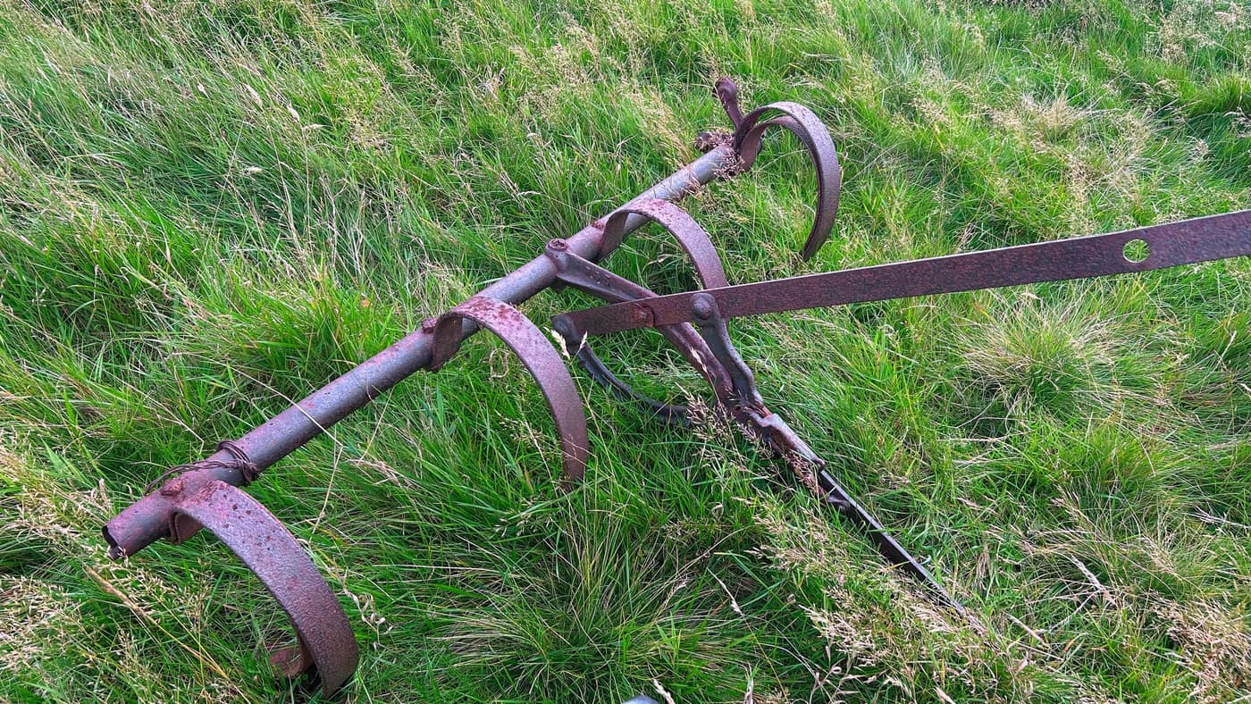 An old horse-drawn implement rusting into the grass by the wall
