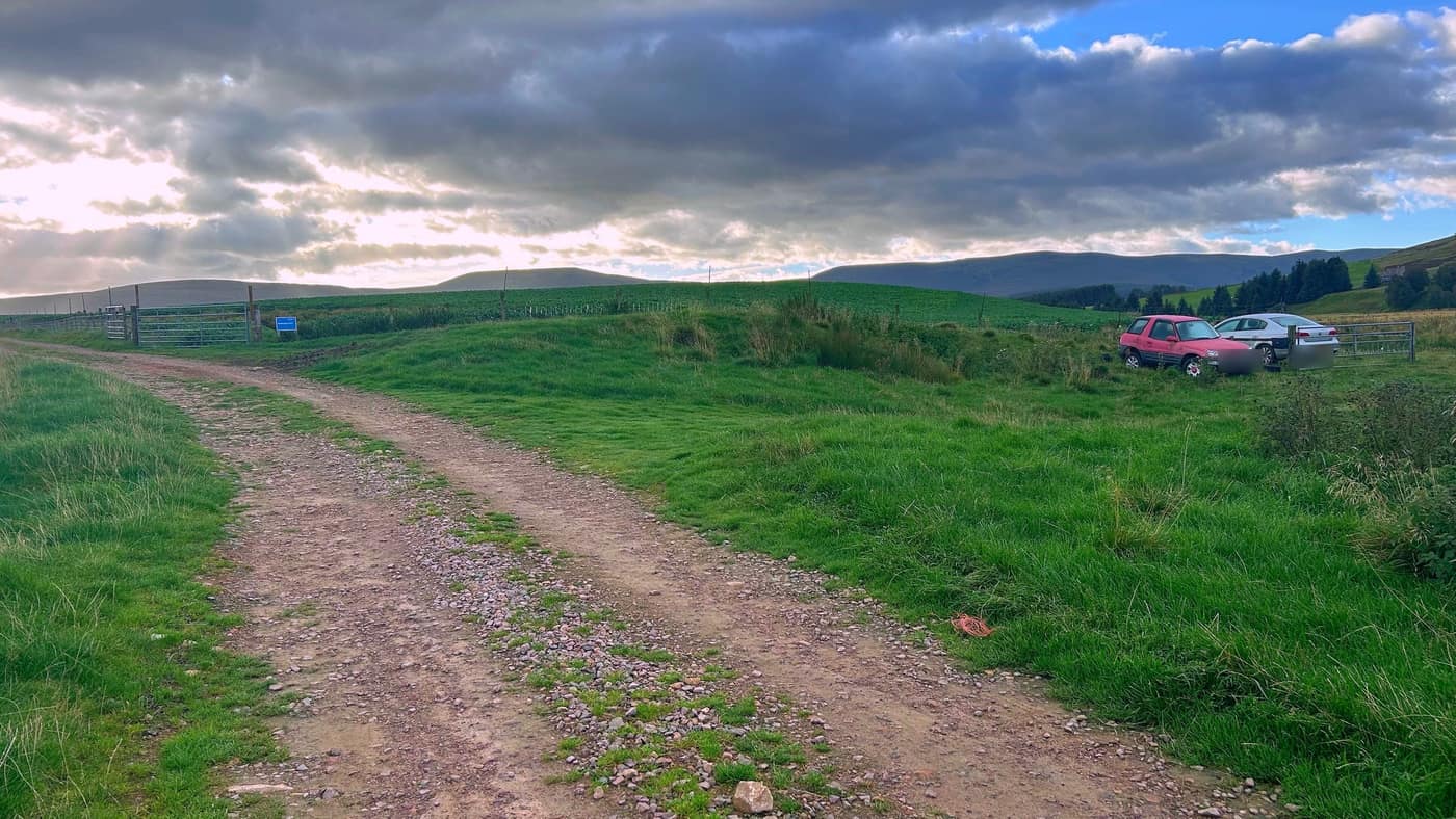 The track on, with the parked cars by the gate marking where the path drops to the bridge