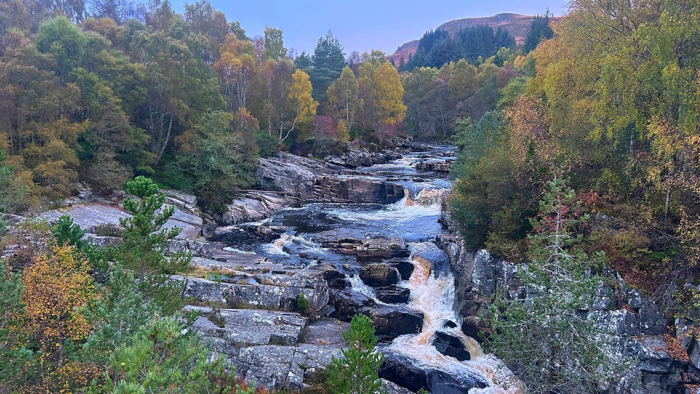 The Black Water crashing through the rocks below the bridge, autumn trees either side