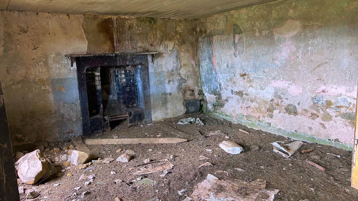 A cast iron fireplace still in the wall, earth and rubble on the floor