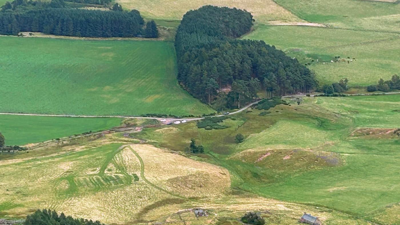 Zoomed in on the car park, the cars small on the track, with the derelict house below