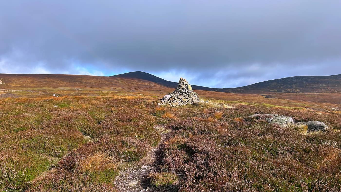 A cairn beside the path, the summit cone of Mount Keen behind it
