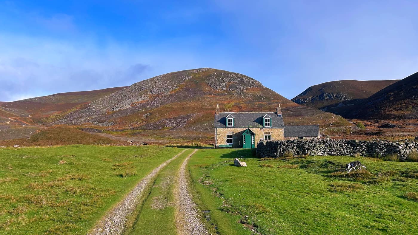 The lodge at the foot of the hill, drystone wall round it and a green door
