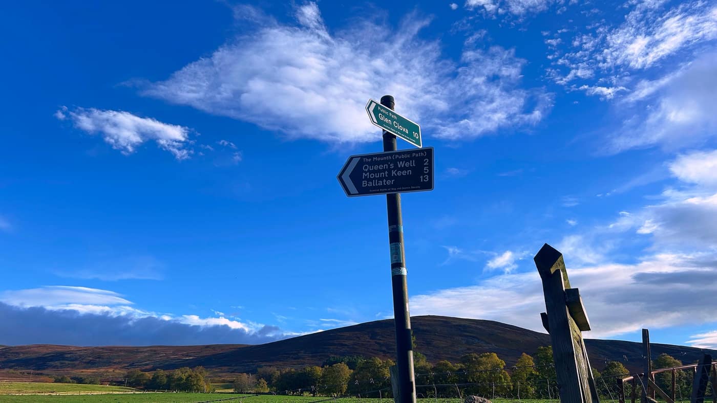 The signpost against a blue sky — Glen Clova one way, the Mounth path with Queen's Well and Mount Keen the other