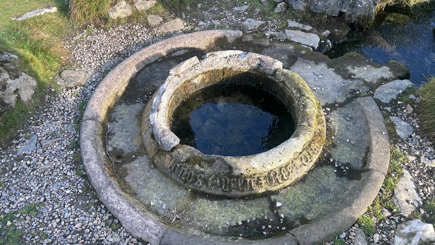 The stone basin of the well, water still in it, the worn inscription round the rim