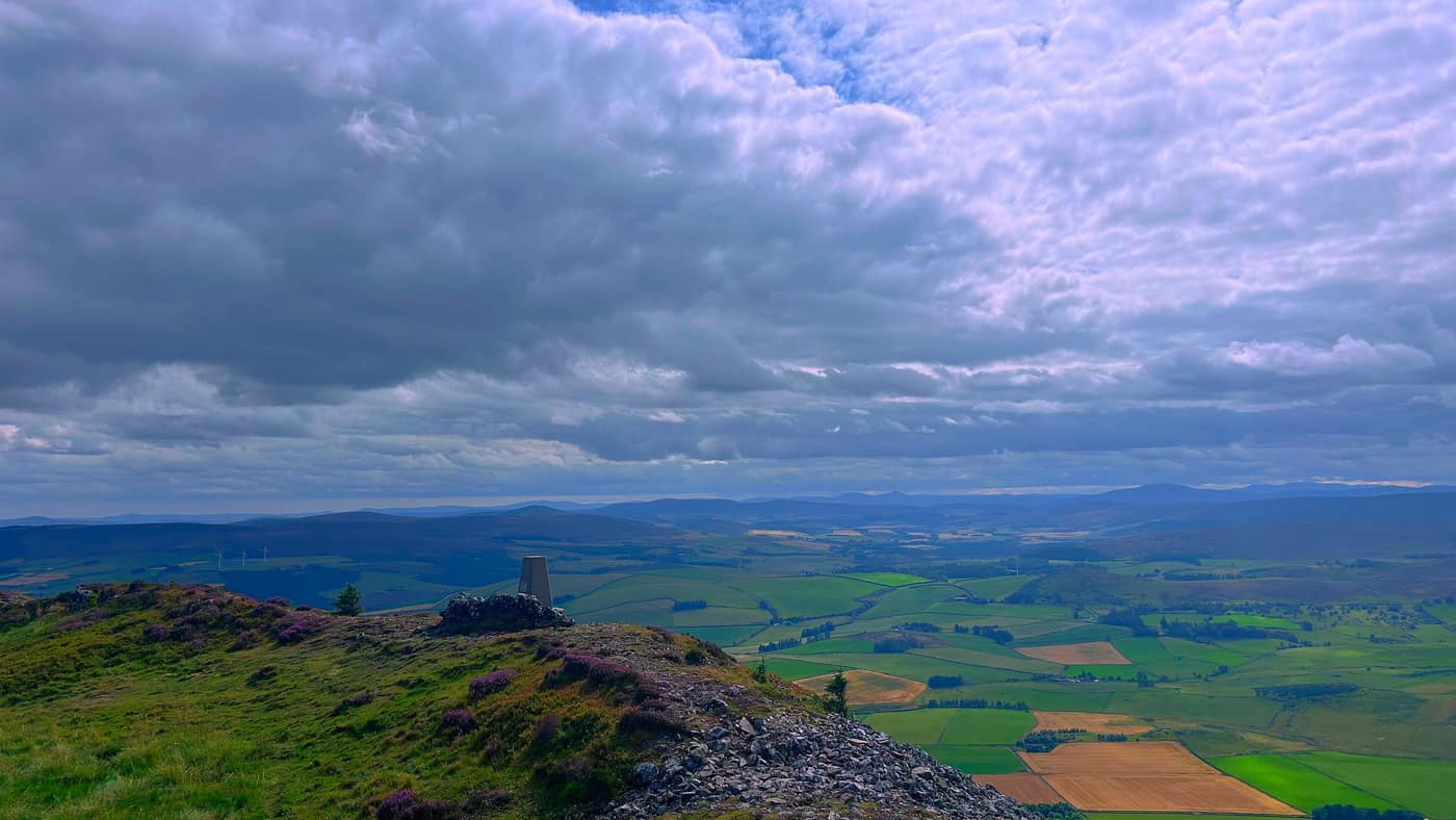 The trig point sitting on the end of the ridge with the fields below