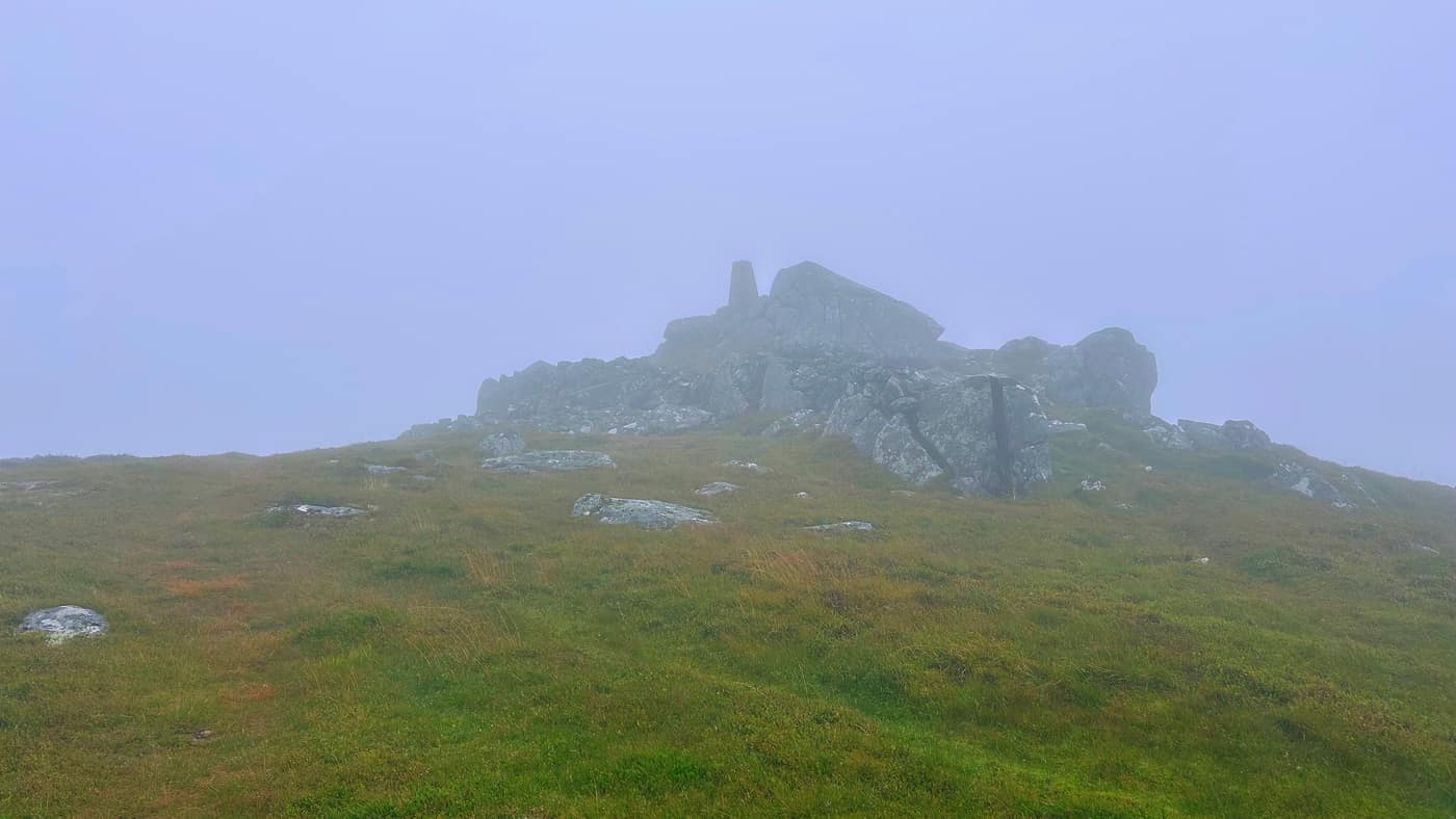 The summit rocks coming out of the mist with the trig point on top of them